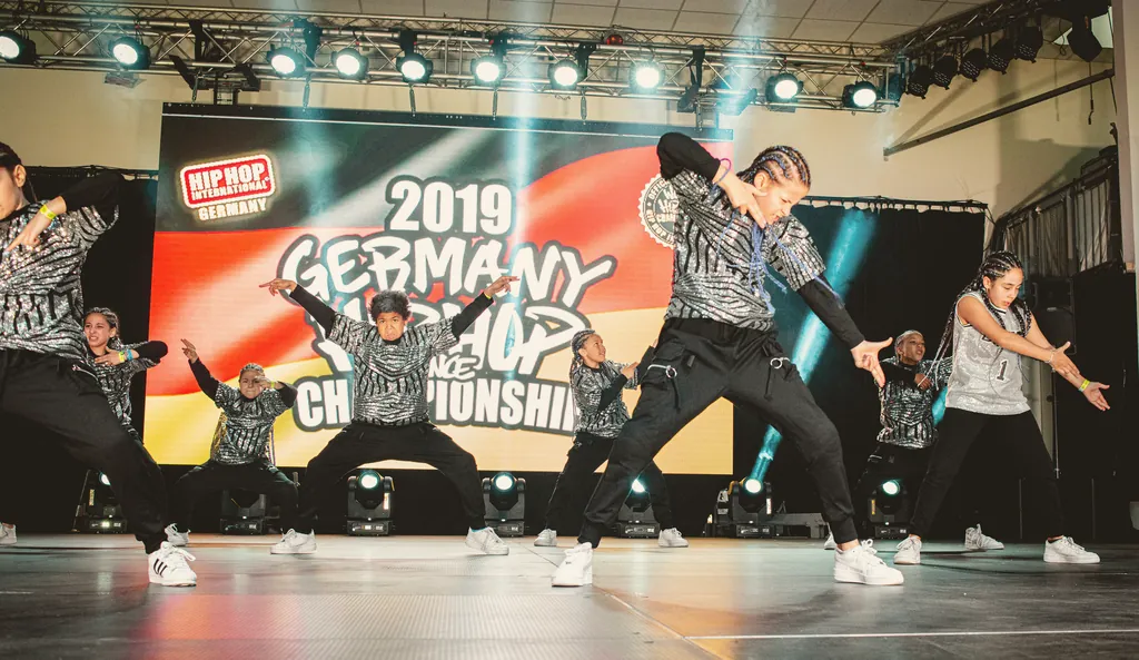 Crew in silver outfits in front of the Germany Hip Hop Dance Championship 2019 banner