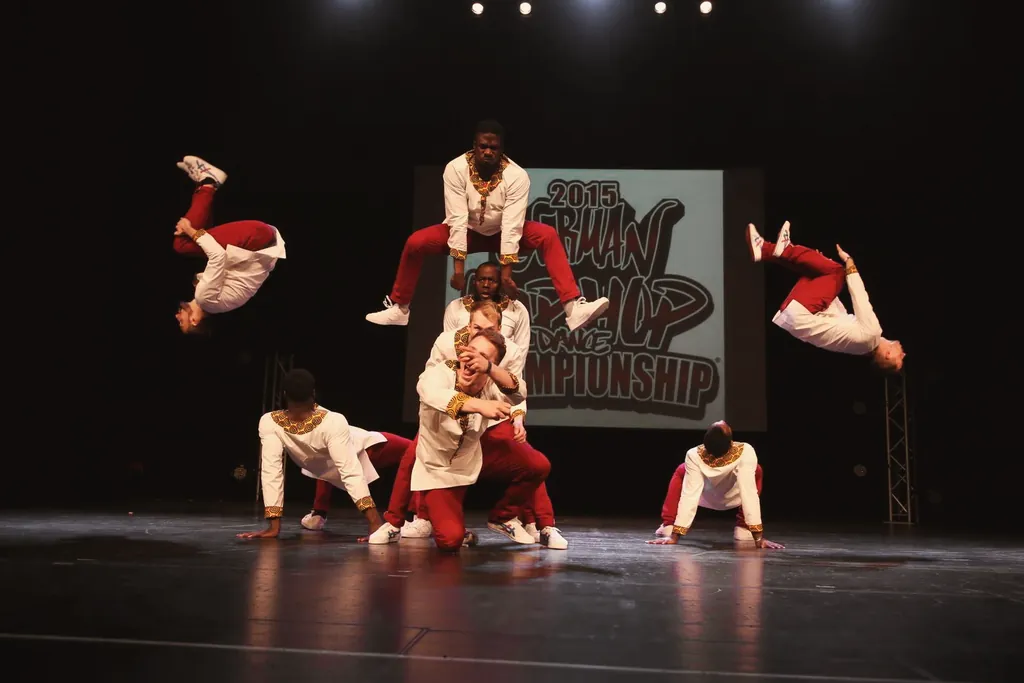 Crew in white and red doing flips in front of the German Hip Hop Dance Championship 2015 banner