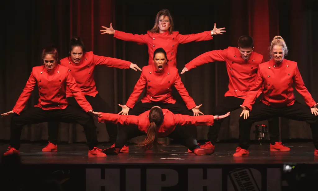 Crew in red jackets in a formation with outstretched arms on the HHI stage