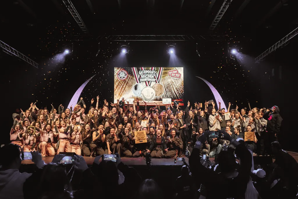 All crews celebrating together on the stage of the Germany Hip Hop Dance Championships, confetti falling, the audience filming on their phones
