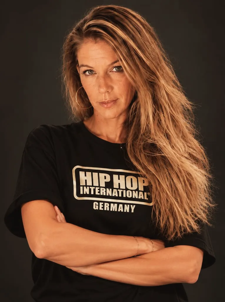 Portrait of Dini, Head of Delegation of HHI Germany, arms crossed, in an HHI Germany shirt