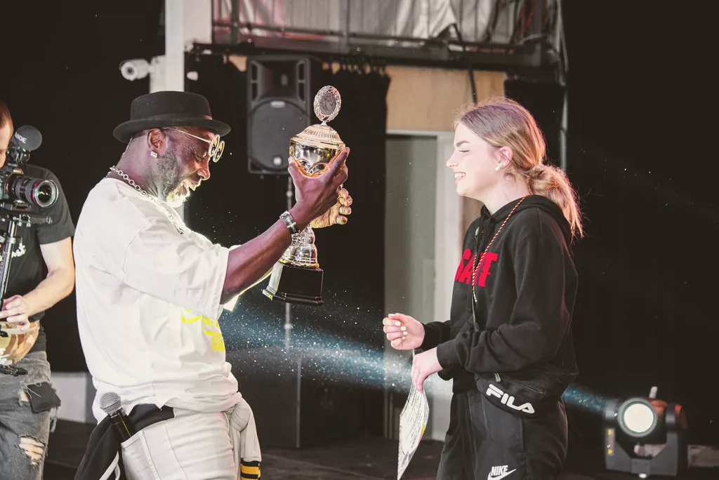 National Director Olando handing a trophy to a young dancer, both laughing
