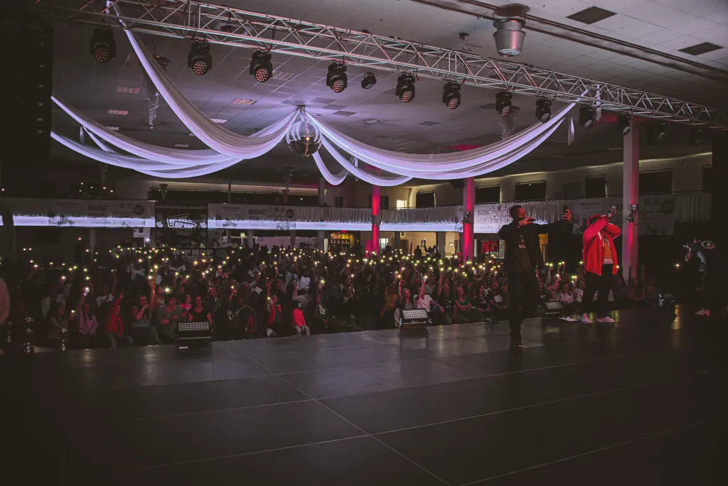 A packed hall at HHI Germany: the audience holds up phone lights, the hosts stand on stage